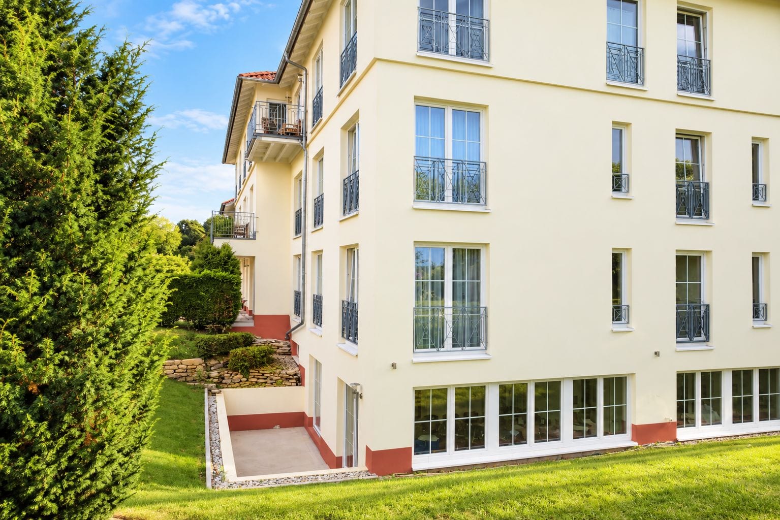 A multi-story building with balconies, a stone staircase, and a well-maintained lawn.