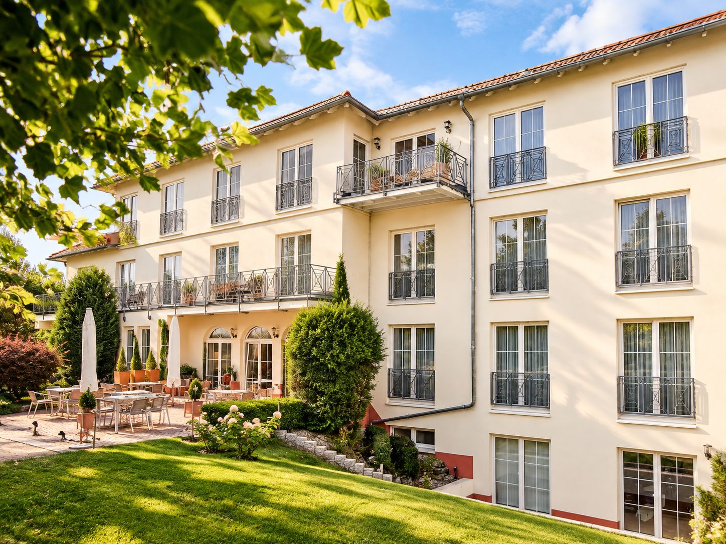 A multi-story building with balconies, outdoor seating, and a well-maintained garden.