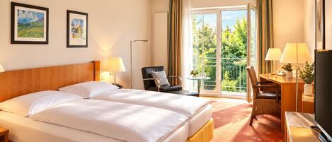 A hotel room with a large bed, a desk with a chair, a television, and a balcony with curtains.