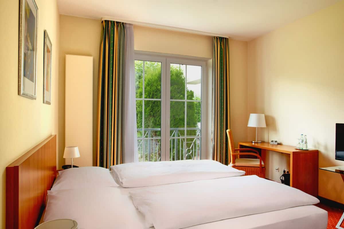 Ein Hotelzimmer mit Bett, Schreibtisch mit Stuhl, Fernseher und einem fenster mit Vorhängen.