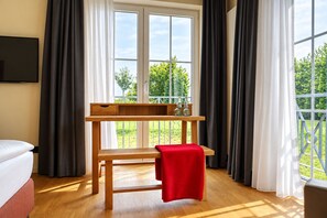 Et værelse med en træbænk, et lille bord med flasker, og udsigt til grøn vegetation udenfor.