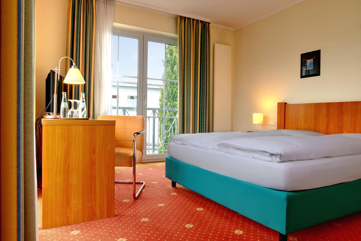 Ein Hotelzimmer mit Bett, Schreibtisch, Stuhl, Lampe und Blick ins Freie.