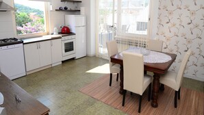 Une cuisine de taille réduite avec des meubles blancs, une cuisinière et un réfrigérateur. On y trouve une table à manger avec des chaises et une fenêtre avec des rideaux.