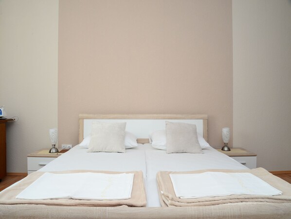 A double bed with a wooden headboard, two bedside tables with lamps, and a neutral-colored wall.