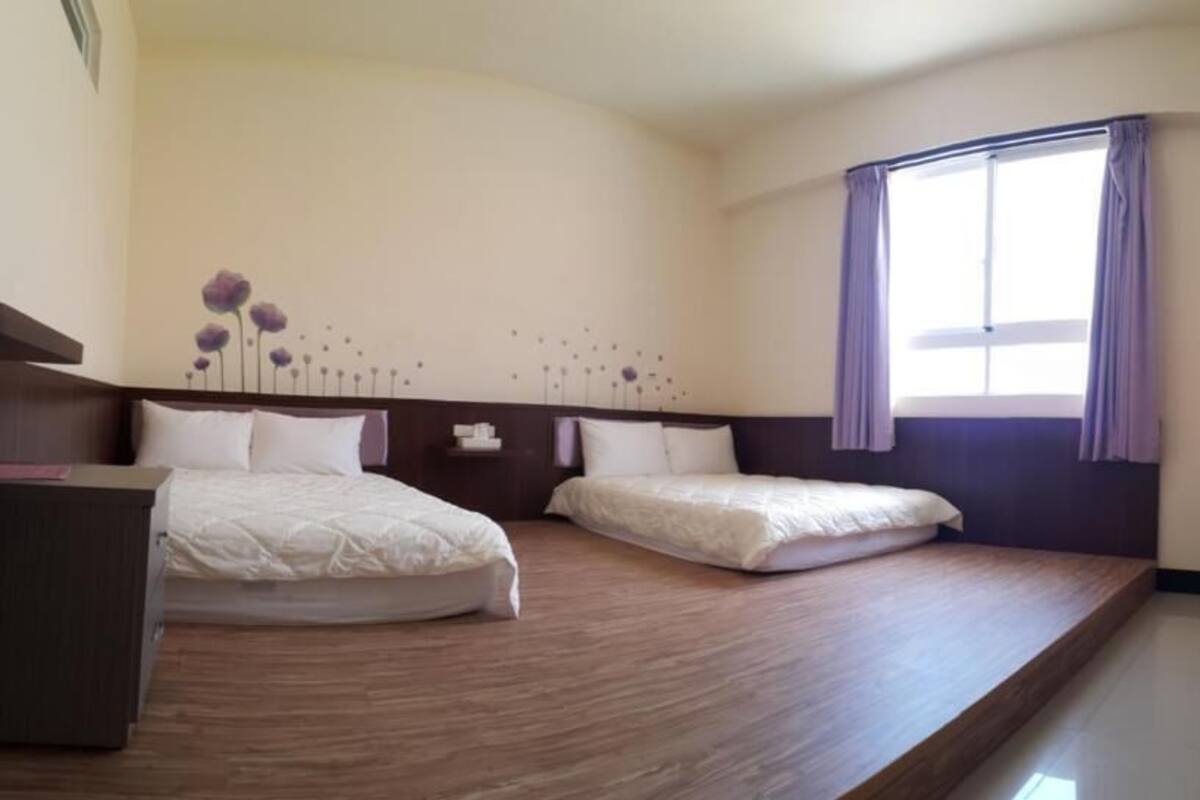 Una habitación de hotel con dos camas, un escritorio, un televisor y una ventana con cortinas.