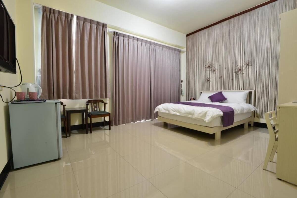 Habitación de hotel con cama, escritorio, silla, un refrigerador pequeño y cortinas.