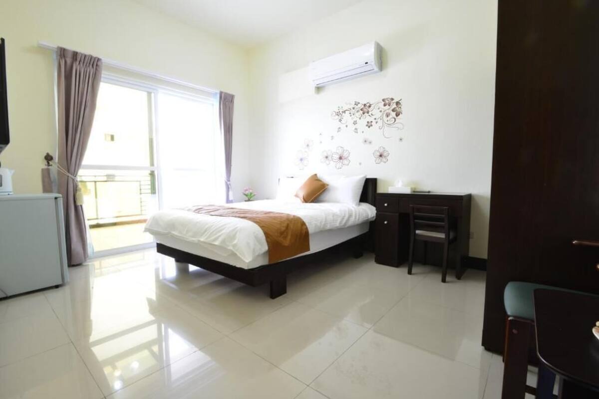 Habitación de hotel con cama, escritorio, silla, cómoda y unidad de aire acondicionado en la pared.