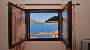 A room with a window offering a view of a body of water and a distant mountain. - South Island Apartments (Korcula)