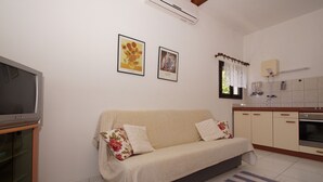 A living room with a sofa, a flat-screen TV, and a kitchen area with a stove and cabinets. - South Island Apartments (Korcula)