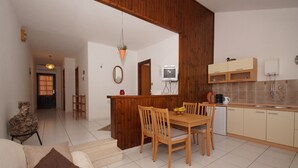A living room with a wooden dining table, chairs, a sofa, and a TV in the corner. - South Island Apartments (Korcula)