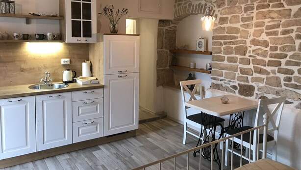 Una cocina con armarios blancos, encimera de madera y pared de piedra.
