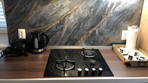 Una cocina moderna con salpicadero de mármol negro, estufa a gas, cafetera y una bandeja de tazas de té.