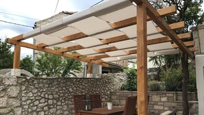 Una pérgola de madera con un muro de piedra y una mesa con sillas debajo.
