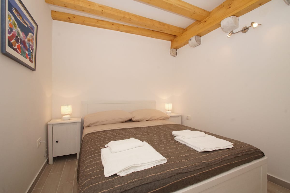 A bedroom with a bed, two bedside lamps, a nightstand, and a framed picture on the wall.