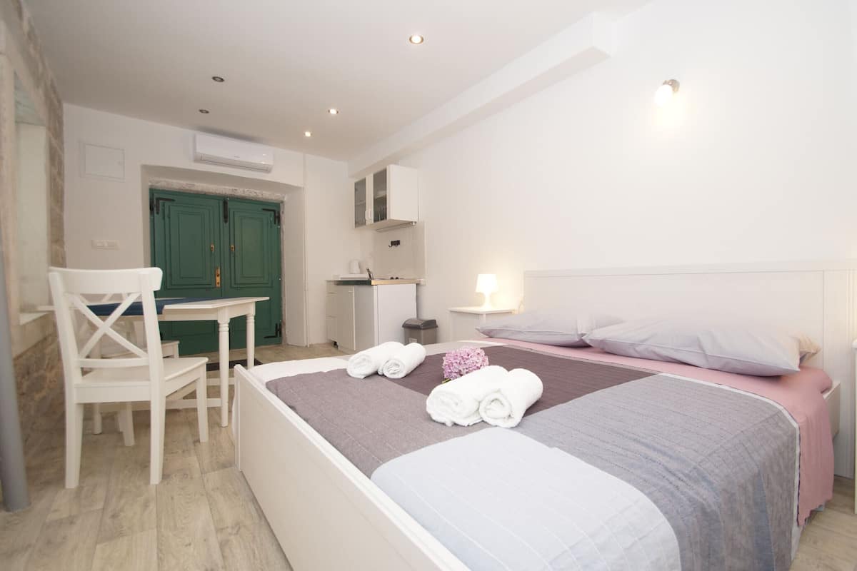 A bedroom with a bed, a chair, a table, and a green door.