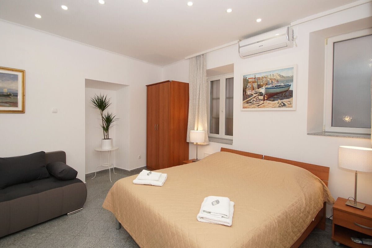 A hotel room with a bed, a sofa, a potted plant, a wardrobe, and a painting on the wall.