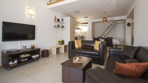 A modern living room with a flat-screen TV, a dark leather sofa, a coffee table, and a staircase leading to an upper level. - Oasis Blue (Korcula)