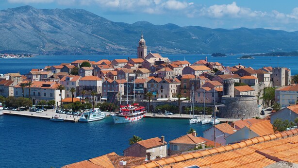 A coastal town with historic buildings, a prominent tower, and a waterfront marina. - Oasis Blue (Korcula)