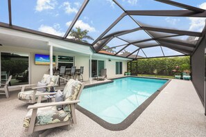 An indoor swimming pool with lounge chairs, a covered patio, and a view of the outdoors.