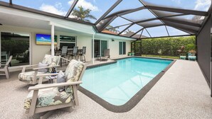 An indoor swimming pool with lounge chairs, a covered patio, and a view of the outdoors. - Nautical home w/ pool, grill & steps to shops (Marco Island)