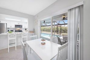 A modern kitchen with white cabinetry, a built-in microwave, and a dining area with a white table and chairs. - Nautical home w/ pool, grill & steps to shops (Marco Island)