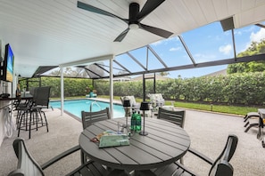 An outdoor patio with a pool, covered seating, and a table with items on it. - Nautical home w/ pool, grill & steps to shops (Marco Island)