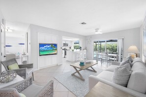 A modern living room with a flat-screen TV, a sofa, and a dining area with a kitchen in the background. - Nautical home w/ pool, grill & steps to shops (Marco Island)
