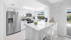 A modern kitchen with white cabinetry, stainless steel appliances, and a central island with seating. - Nautical home w/ pool, grill & steps to shops (Marco Island)