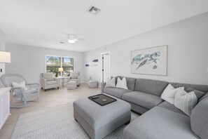 A modern living room with a grey sofa, armchairs, a coffee table, and a large window with blinds.