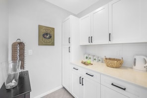 A kitchen with white cabinets, a glass of water, a wicker basket, and a white kettle. - Nautical home w/ pool, grill & steps to shops (Marco Island)