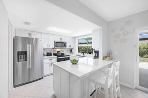 A modern kitchen with a central island, stainless steel appliances, and a view to the outdoors. - Nautical home w/ pool, grill & steps to shops (Marco Island)