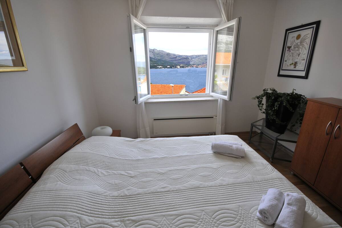 Quarto com uma cama grande, janela com vista para o mar, armário de madeira e um quadro na parede.