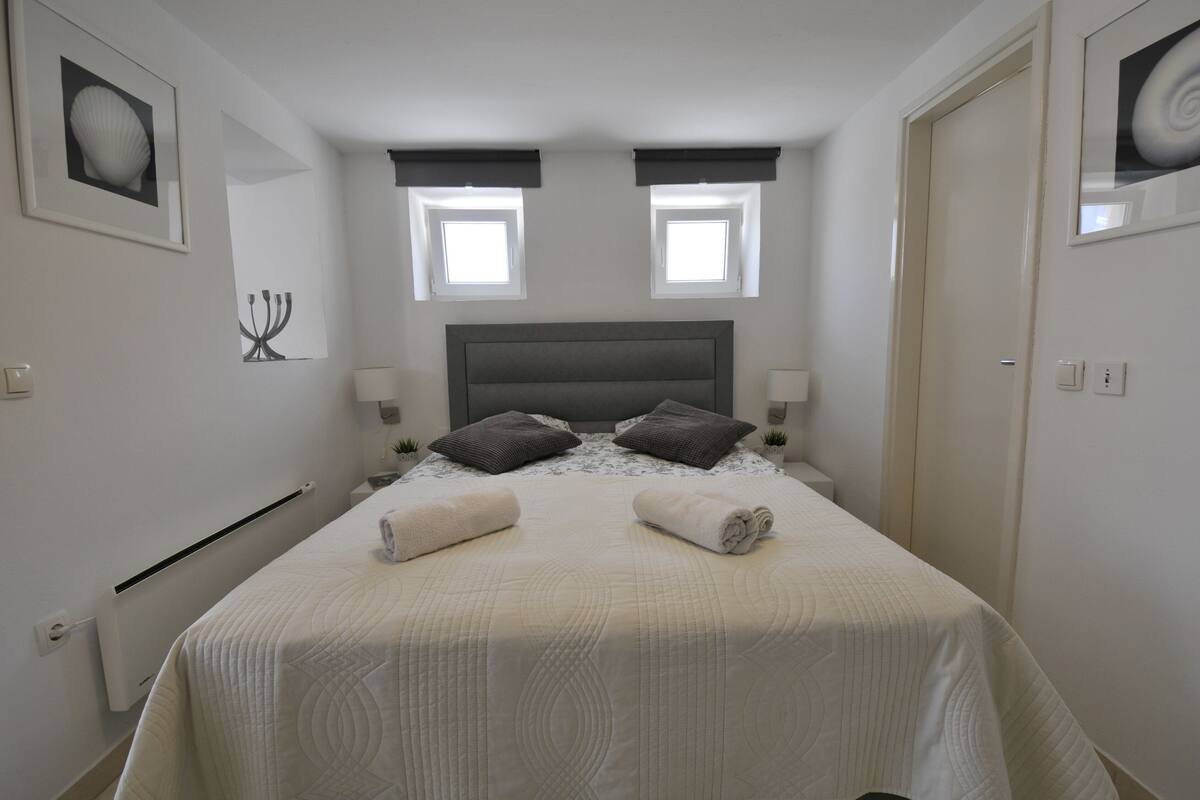 Cama bem arrumada com almofadas, duas luminárias de cabeceira e encosto.