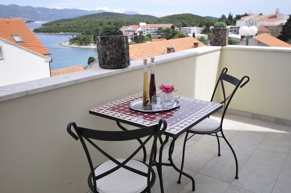 A balcony with a table and chairs, a potted plant, and a view of a body of water and buildings in the background.