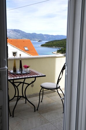 A balcony with a table, two bottles, a glass, and a flower arrangement.