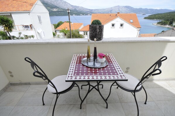 A balcony with a table and chairs, a potted plant, and a scenic view of a lake and mountains.