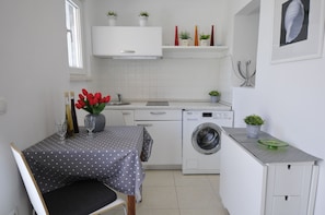 A compact kitchen with a washing machine, a dining table with a polka dot tablecloth, and a window. - Bella Vita (Korcula)