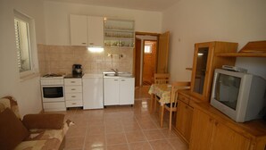 A compact kitchen with a stove, sink, and refrigerator. There's a dining table with chairs and a television on a wooden cabinet. - Vita Apartments (Korcula)