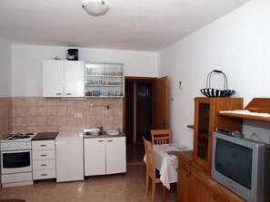 Una cocina compacta con armarios blancos, una estufa, un fregadero y una zona de comedor con mesa y sillas.