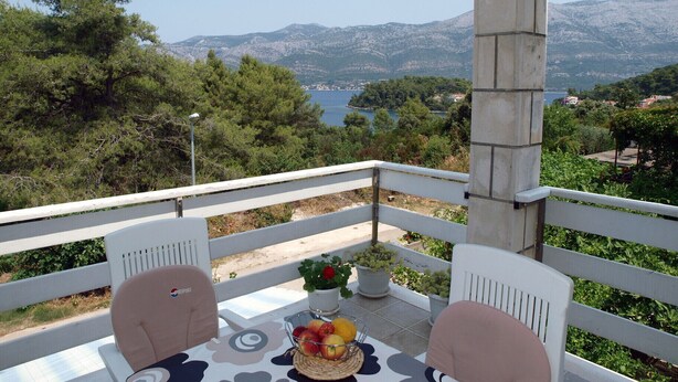 A balcony with a table set for two, overlooking a scenic view of mountains and a body of water. - Vita Apartments (Korcula)