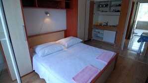 A bedroom with a bed, a built-in wardrobe, and a kitchenette area. - Vita Apartments (Korcula)