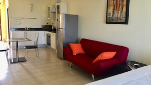 Un espacio habitable compacto con kitchenette, comedor y sofá rojo con cojines naranjas.