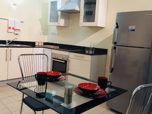 A compact kitchen with a refrigerator, oven, and a dining table with chairs.
