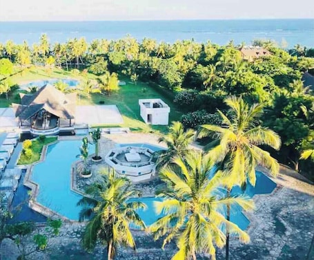 An aerial view of a resort with multiple swimming pools, palm trees, and a view of the ocean.