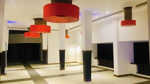 Un vestíbulo espacioso con diseño moderno, que presenta una columna central y múltiples lámparas rojas colgantes.