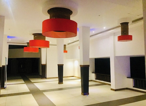 A spacious lobby with a modern design, featuring a central column and multiple hanging red light fixtures.