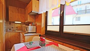 A compact kitchen with wooden cabinets, a microwave, and a window with blinds. - Willa u Bachledów (Zakopane)