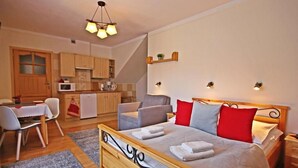 A bedroom with a wooden bed, a small kitchenette, a dining area, and a living space. - Willa u Bachledów (Zakopane)