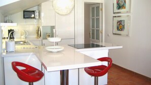 A modern kitchen with a white countertop, two red bar stools, a hanging light fixture, a microwave, and a door leading to another room.