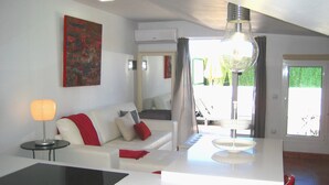 A modern living room with a white sofa, red cushions, a black table, and a large window with a view of the outdoors.